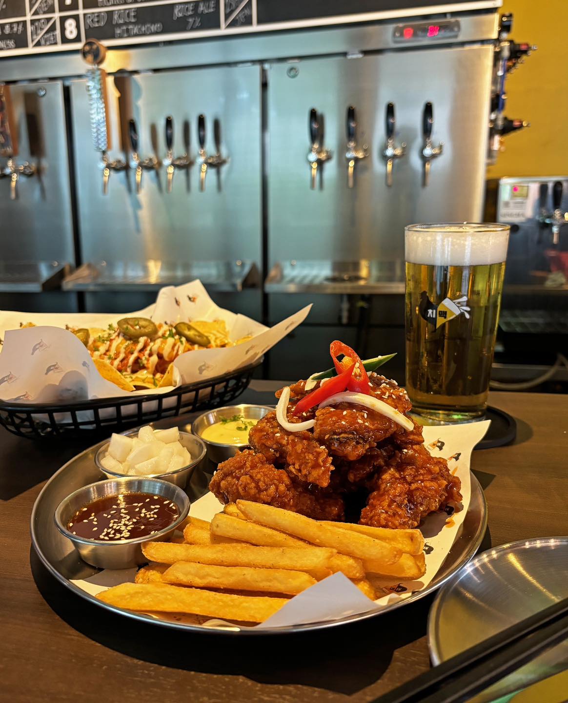The exterior storefront of the "Beer & Chicken" restaurant, featuring large bold signage and a promotional poster for craft beer and Korean fried chicken. The glass entrance reflects the urban street scene.